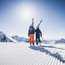 Zwei Skifahrer mit Skiern auf verschneiter Bergpiste bei sonnigem Wetter