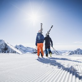 Zwei Skifahrer mit Skiern auf verschneiter Bergpiste bei sonnigem Wetter