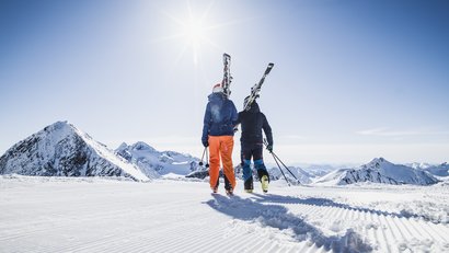 Zwei Skifahrer mit Skiern auf verschneiter Bergpiste bei sonnigem Wetter