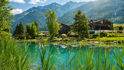 Berglandschaft mit See, grünen Bäumen und modernen Gebäuden im Sonnenschein