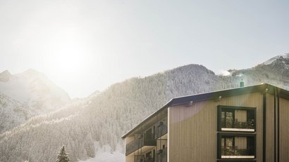 Holzhaus vor schneebedecktem Bergwald bei Sonnenlicht