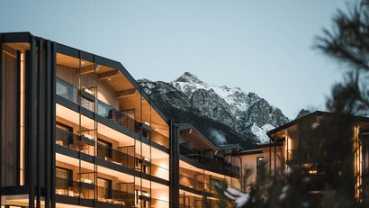 Modernes Gebäude mit beleuchteten Balkonen vor schneebedecktem Berg