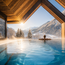 Person im warmen Pool mit Blick auf verschneite Berge durch eine Holzkonstruktion