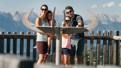 Familie beobachtet Landschaft durch ein Fernrohr auf einem Aussichtspunkt mit Bergkulisse